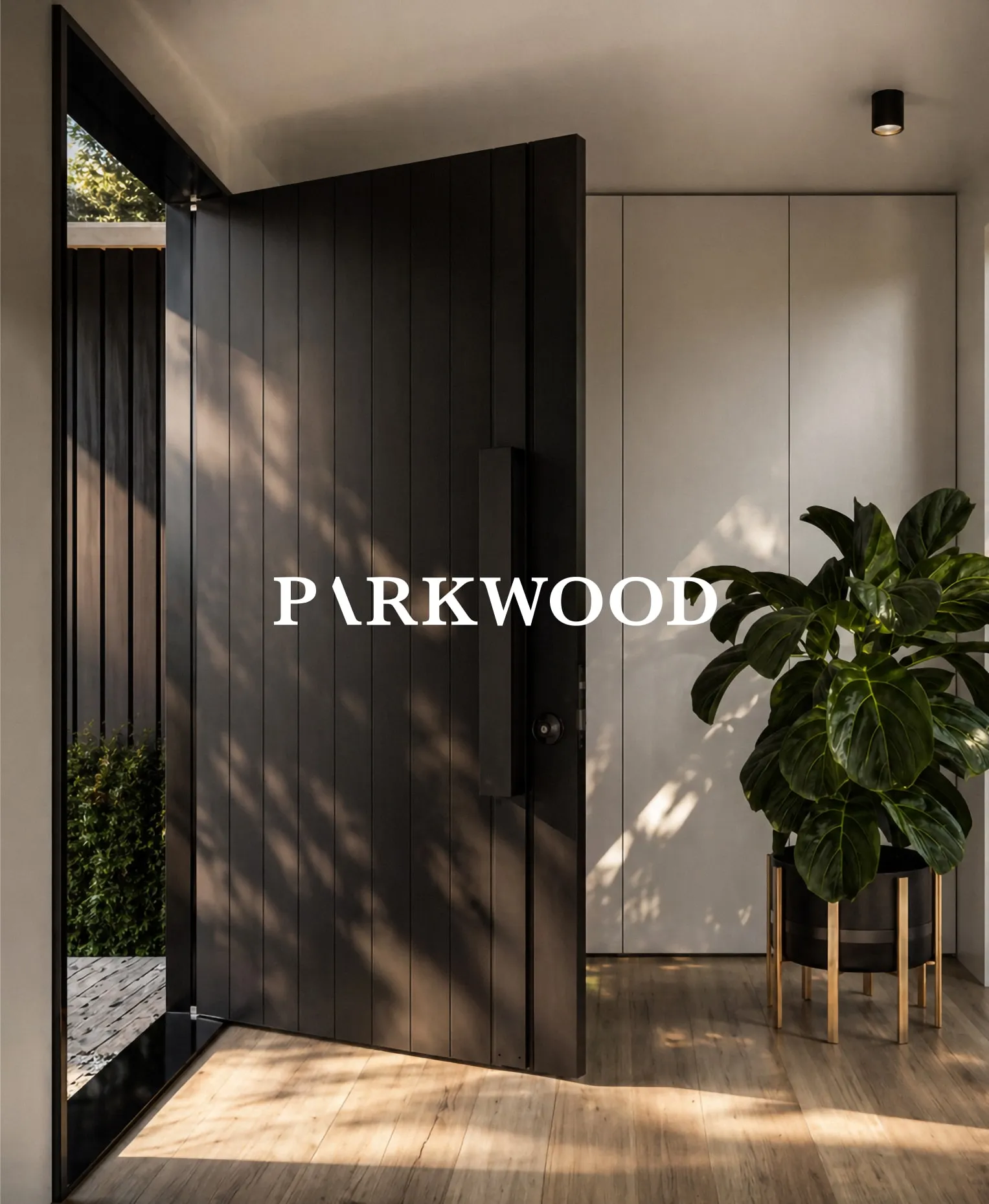 Parkwood: a tall black timber pivot front door standing open into a sunlit hallway with a potted fiddle-leaf fig