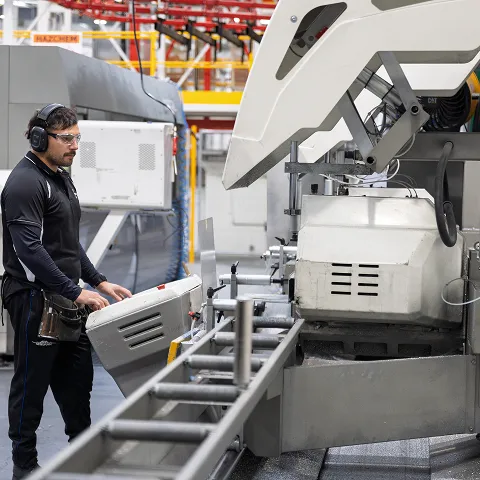 A worker wearing ear defenders operating a large saw on the factory floor