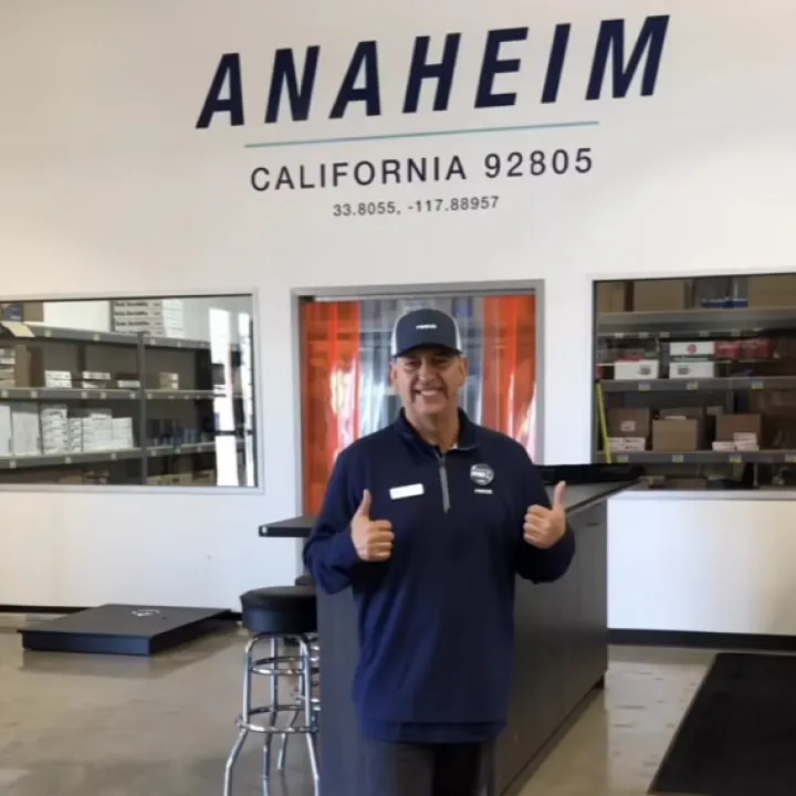 A Reece team member giving two thumbs up inside a branch, under a wall sign reading “Anaheim, California 92805”