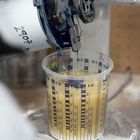Yellow finish being dispensed from a machine nozzle into a graduated mixing cup