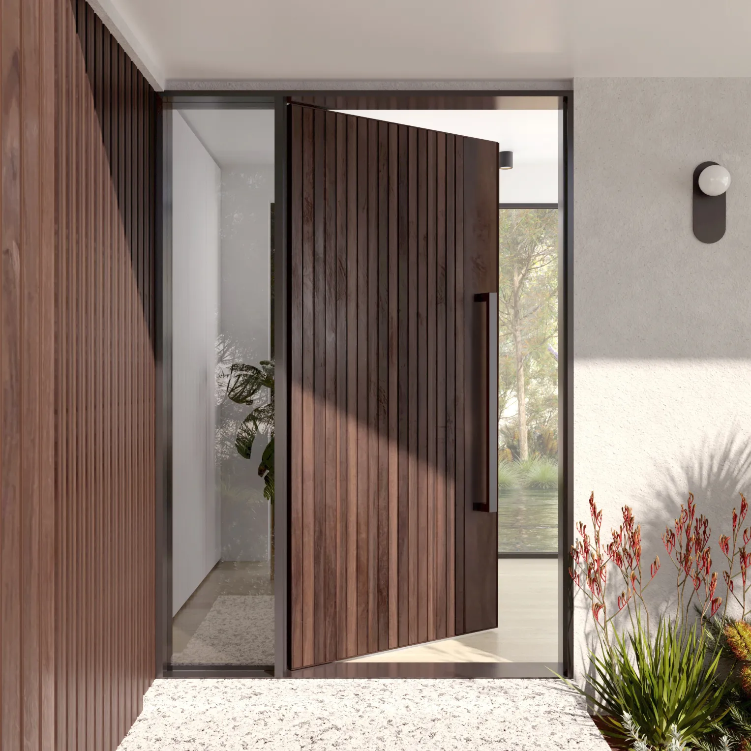 A tall timber-clad pivot front door standing open in a white entry with red-flowering plants