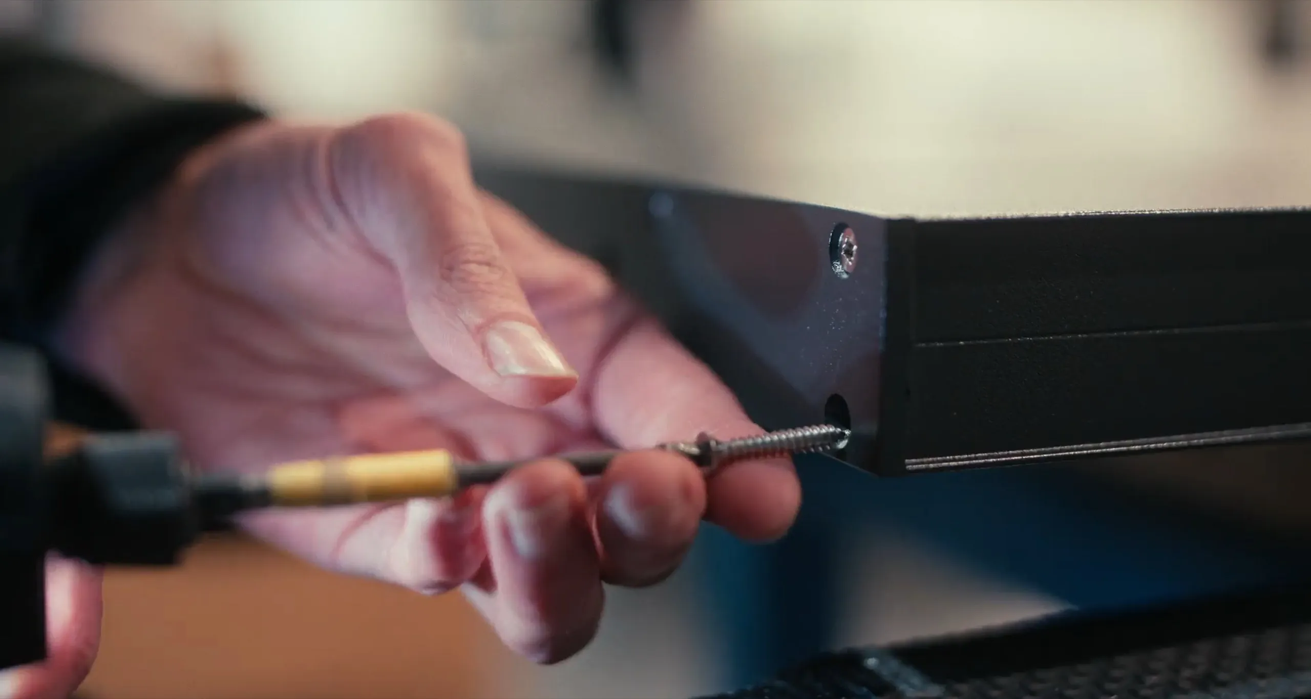A hand driving a screw into the frame of a black aluminium door with a power drill
